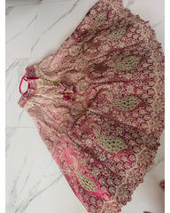 A pink and gold embroidered skirt with intricate lace and sequin detailing, laid flat on a white marble-patterned floor.