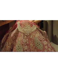 A close-up of a heavily embellished pink and gold traditional bridal gown or lehenga with intricate embroidery and sequins, shown against a dark indoor background.