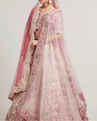 A pink and white heavily embroidered traditional Indian lehenga choli set with a matching dupatta, shown on a model against a plain light gray background.
