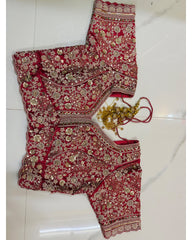 An embroidered red bridal lehenga choli set with intricate gold and silver mirror work, laid flat on a white marble floor, accompanied by a gold chain and red strings.
