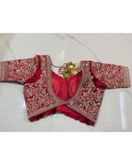 Back view of a red and gold embroidered traditional Indian blouse (choli) with a sweetheart neckline, laid flat on a white marble surface.