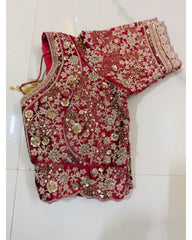 A red embroidered bridal blouse with intricate gold sequin and beadwork, laid flat on a light-colored tiled floor.