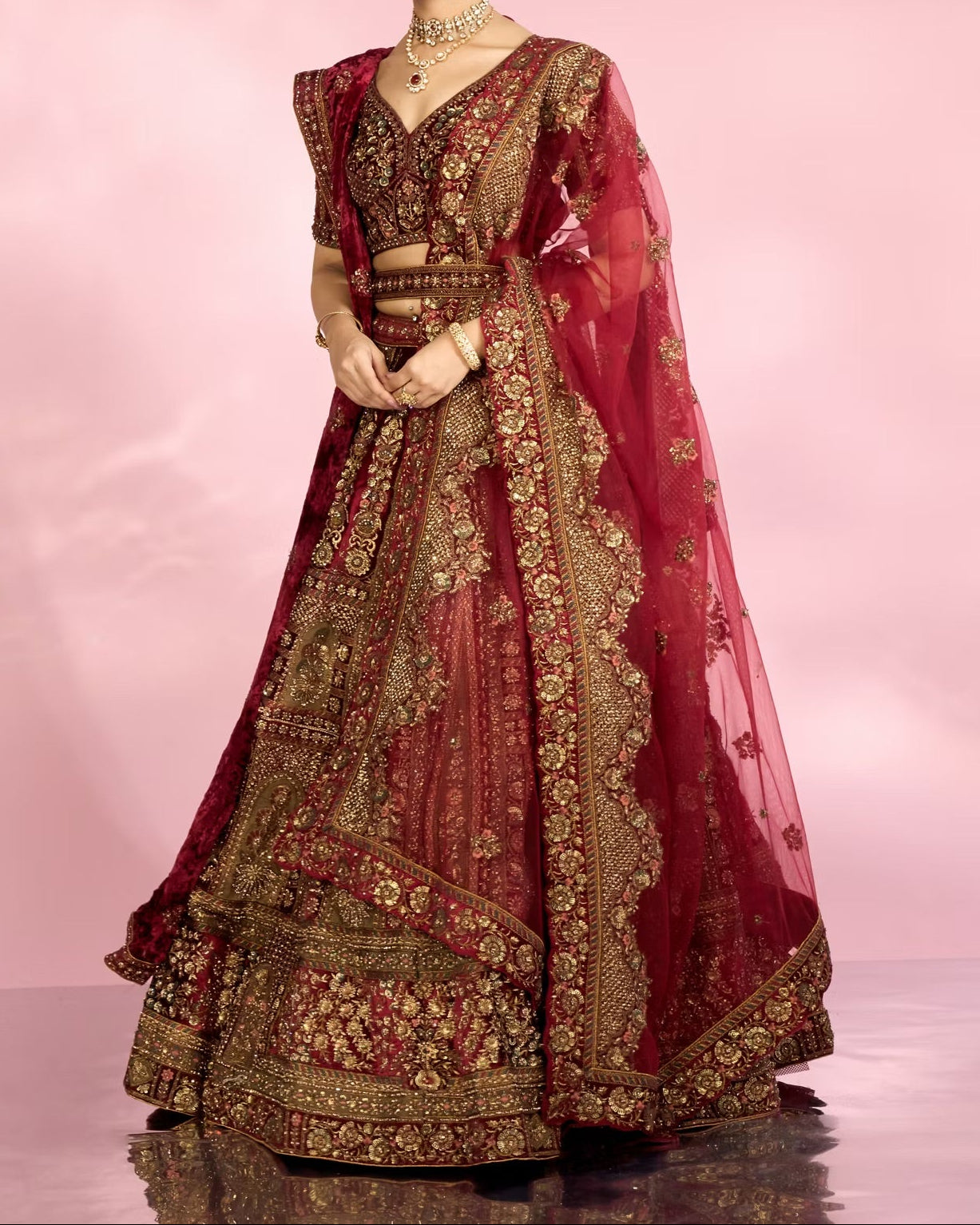Woman wearing a traditional maroon and gold embroidered outfit on a pink background