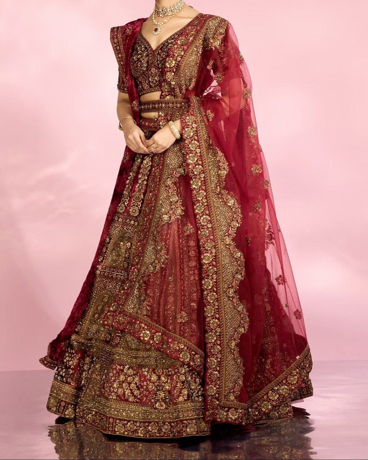 Woman wearing a traditional maroon and gold embroidered outfit on a pink background