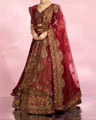 Woman wearing a traditional maroon and gold embroidered outfit on a pink background