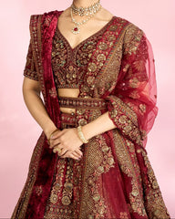 Woman in a traditional maroon and gold embroidered outfit with a pink background
