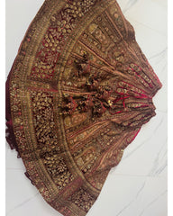 An ornate traditional skirt or lehenga laid flat on a light marble floor, featuring intricate gold zari embroidery, red and gold floral patterns, and heavy bead embellishments.