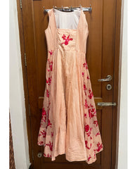 Back view of a sleeveless peach maxi dress with red floral embroidery and a white inner lining, hanging on a clothes rack in front of a wooden door.