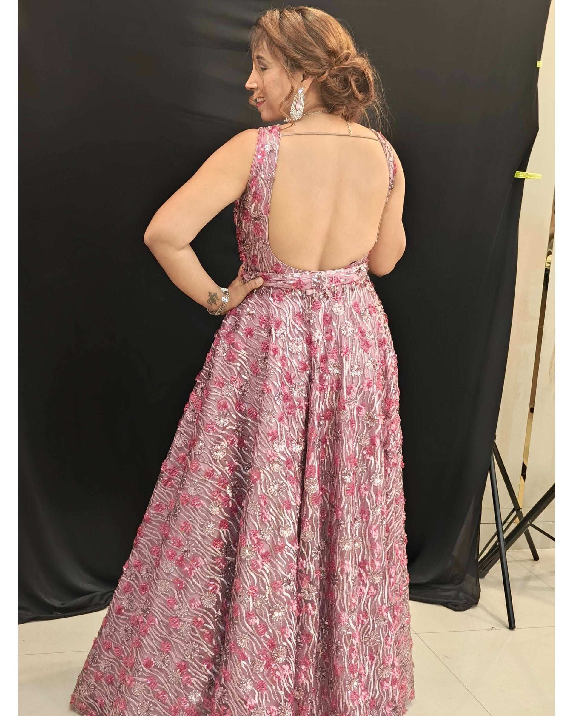 Woman wearing a pink floral dress with an open back, standing against a black backdrop.