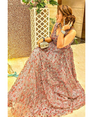 Woman in a floral dress sitting on a decorative chair with a floral arrangement in the background.