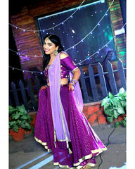 Woman in a purple traditional outfit with a light purple dupatta standing outdoors.