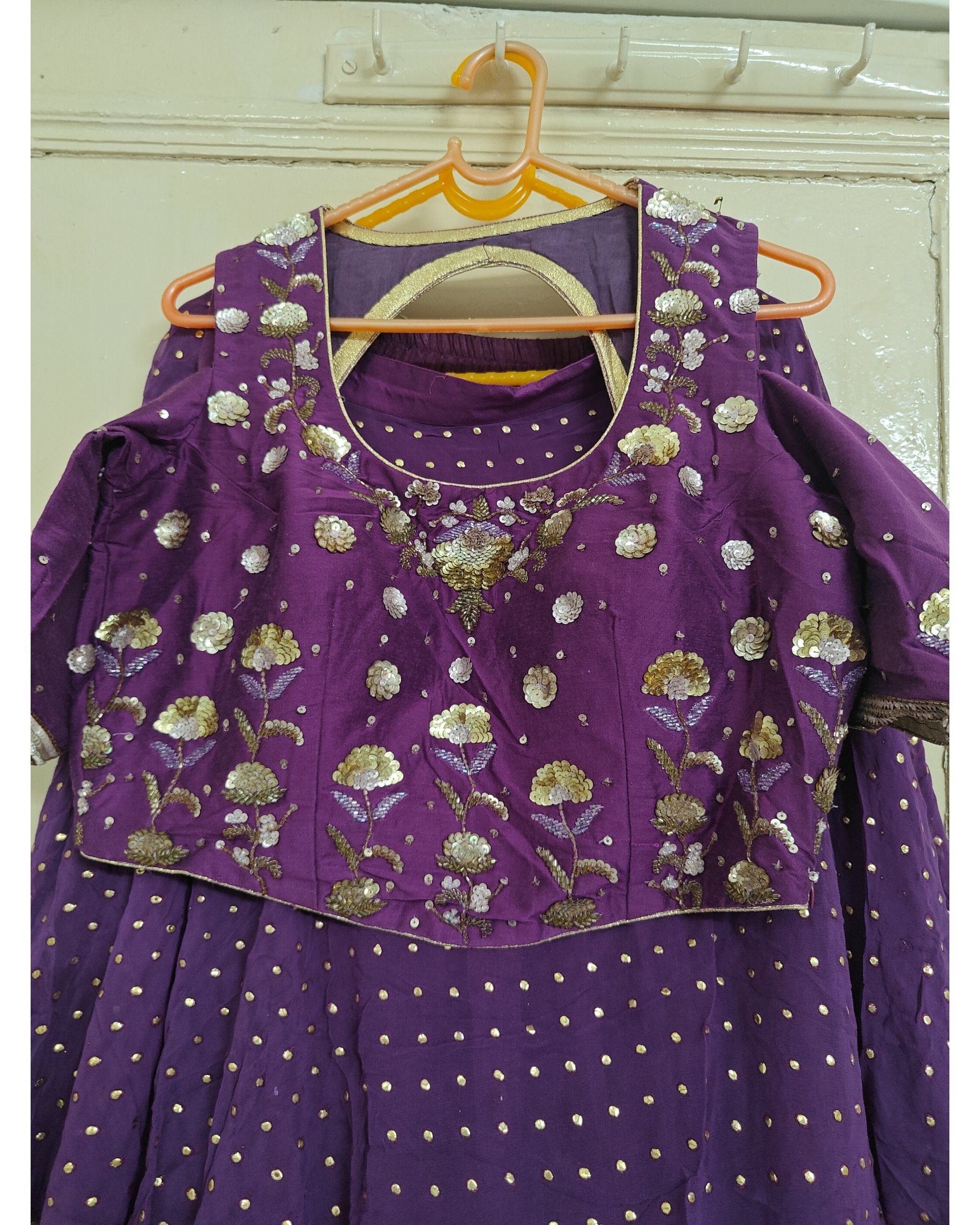 Purple traditional outfit with floral embroidery on a hanger against a white wall.
