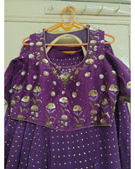 Purple traditional outfit with floral embroidery on a hanger against a white wall.