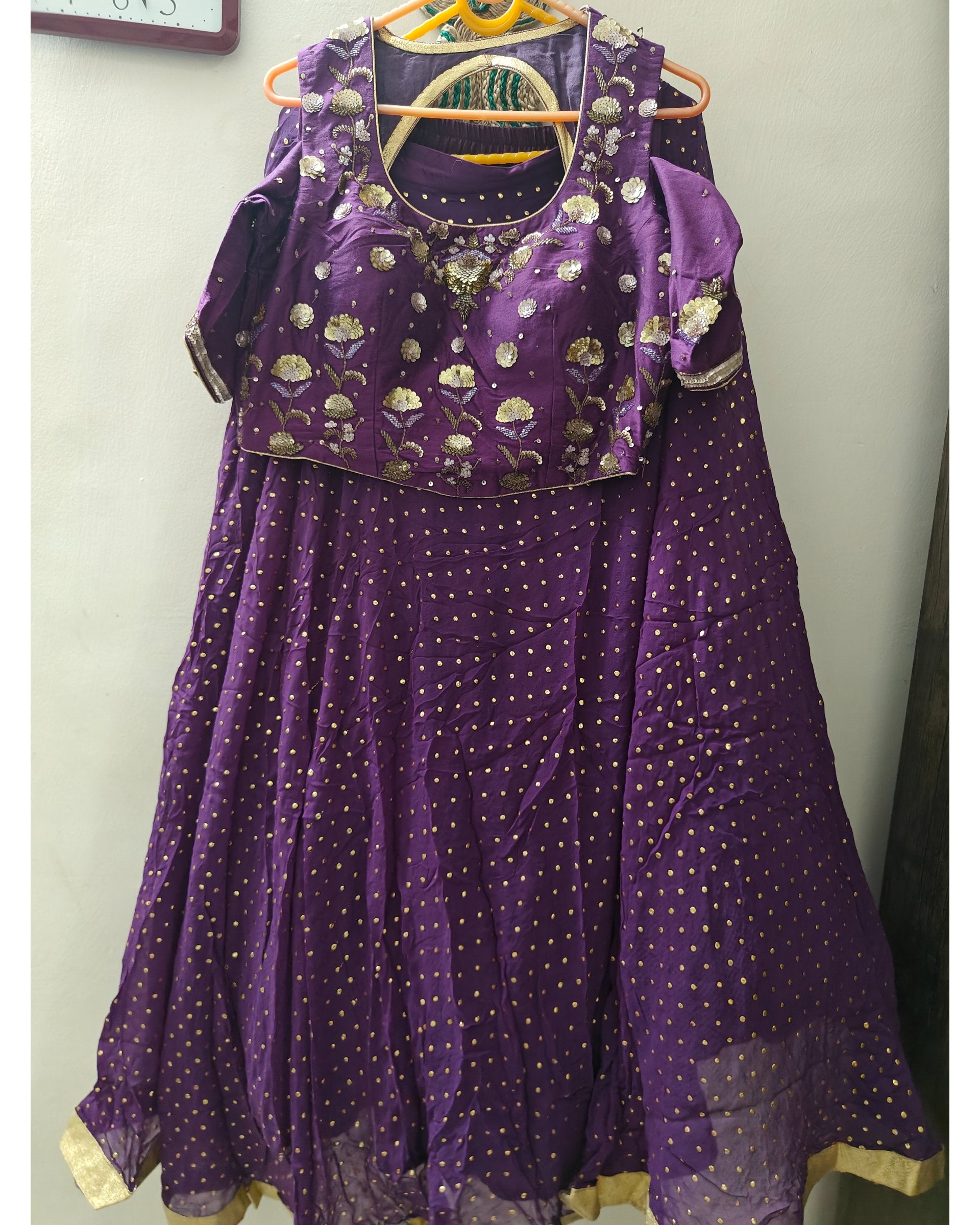 Purple traditional outfit with gold patterns on a hanger against a plain background