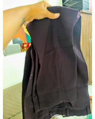 A person's hand holding up a pair of dark purple pants in an indoor setting.