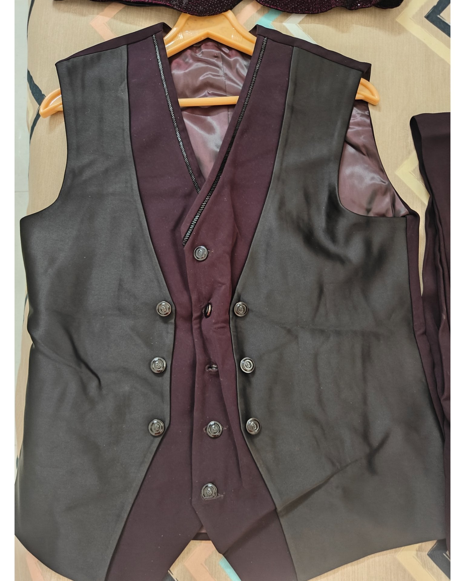 A double-breasted waistcoat vest in a dark charcoal gray fabric with contrasting deep burgundy panels and matching buttons, laid flat on a patterned surface.