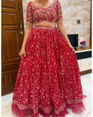 A red and gold embroidered traditional Indian lehenga choli set worn by a model in an indoor setting.