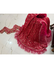 A bright pink and red embroidered traditional lehenga with a matching sheer dupatta and a separate embroidered choli, displayed on a white marble floor.