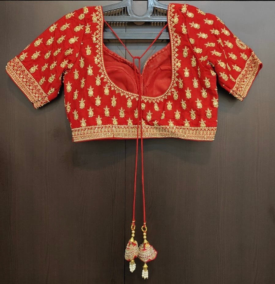 back view of Red embroidered blouse with gold details on a hanger against a dark background
