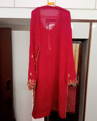 Red traditional outfit with gold embroidery hanging on a rack against a white wall.