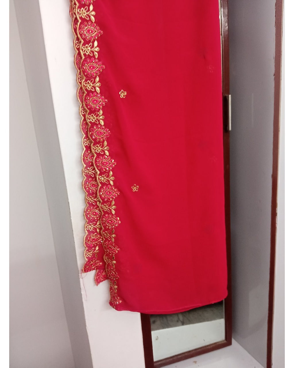 Red fabric with gold embroidery draped over a mirror on a white wall.