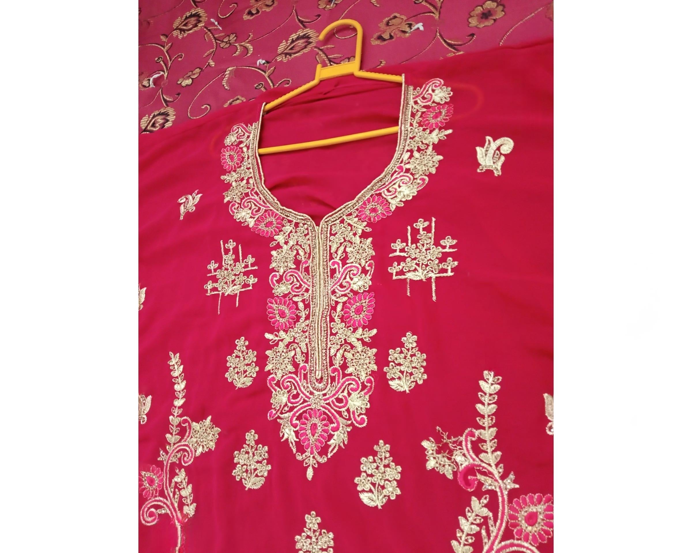 Pink embroidered garment on a hanger against a pink floral background