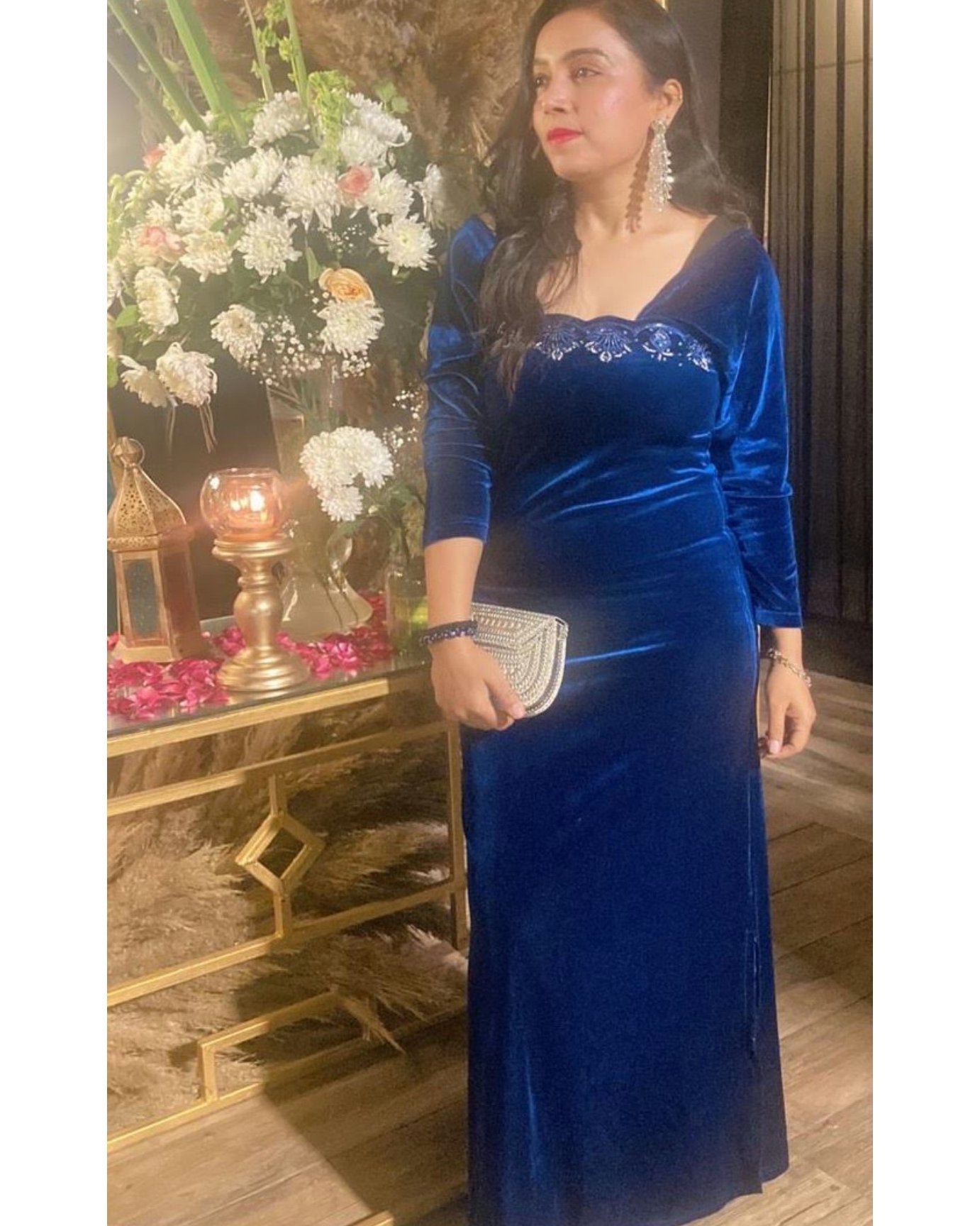 Woman in a blue velvet dress standing in front of a decorated altar.