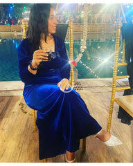 Woman in a blue dress sitting on a chair holding a glass, with a festive background.