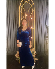 Woman in a blue velvet dress standing in front of a decorative archway with lights.