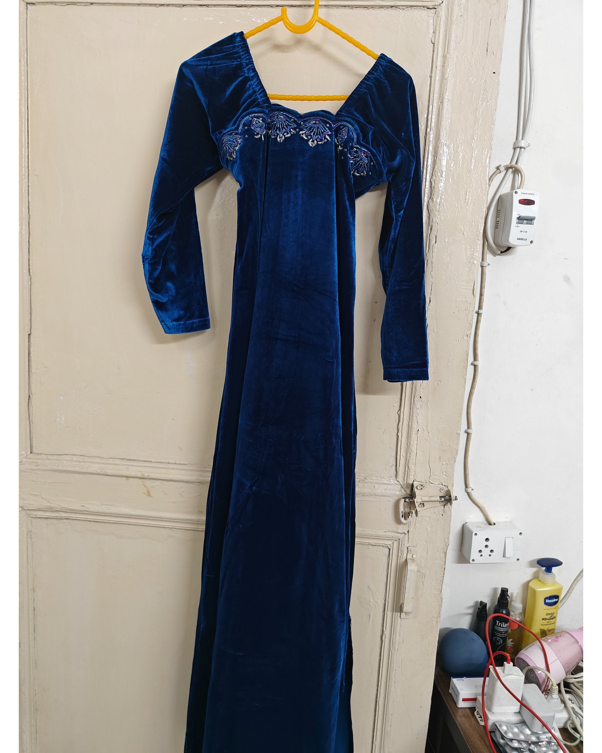Blue velvet dress hanging on a door in a room with visible electrical outlets and a wall socket.