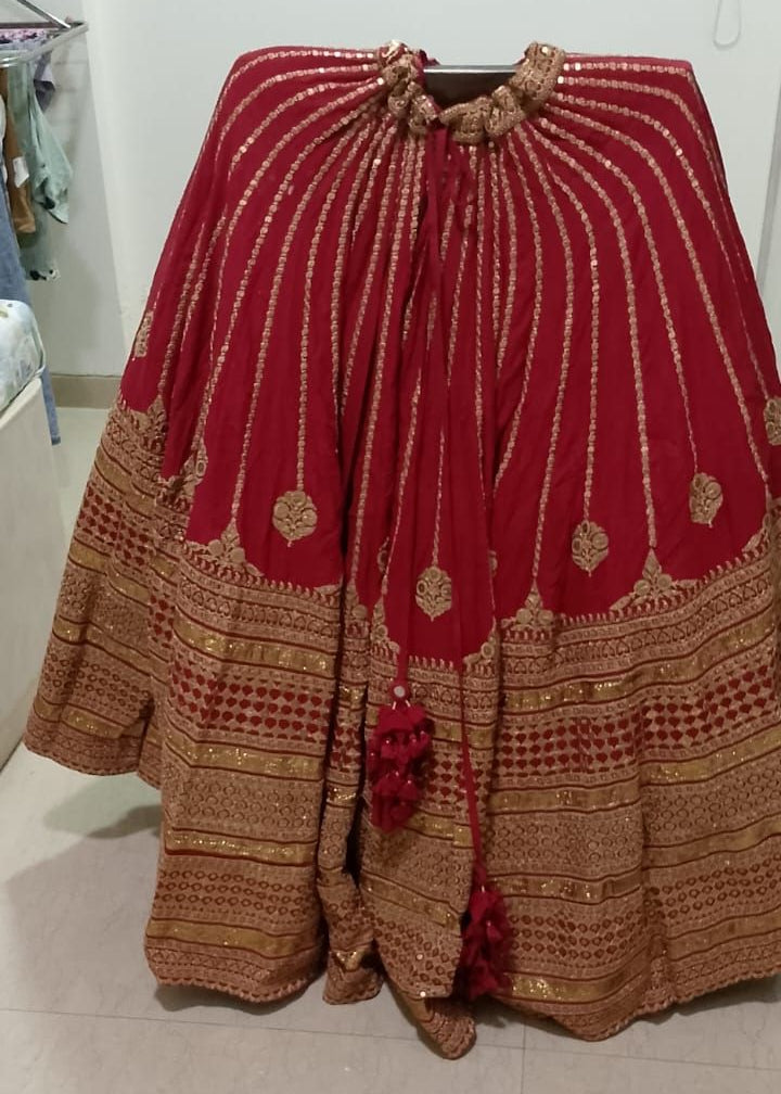 Red and gold traditional Sabyasachi lehenga skirt on a stand against a white wall.