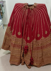 Red and gold traditional Sabyasachi lehenga skirt on a stand against a white wall.
