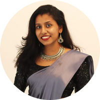 Woman wearing a black blouse with a light purple saree and silver jewelry against a beige background
