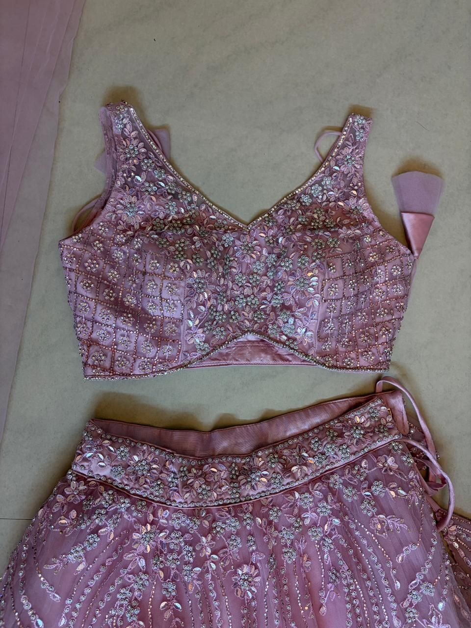 Pink embroidered lehenga choli top and skirt set on a beige surface