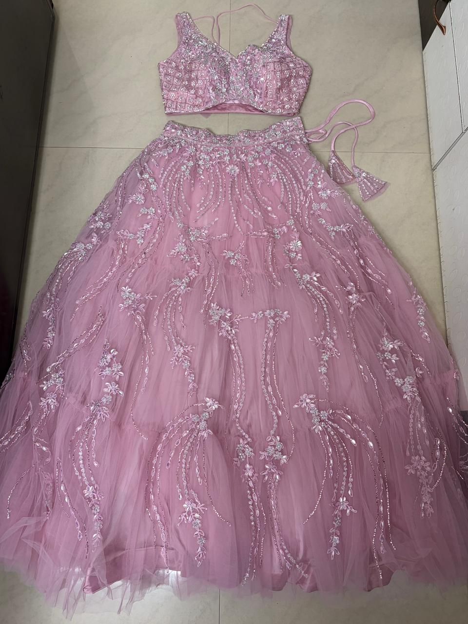Pink lehenga set with floral embroidery on a tiled floor