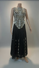 Mannequin wearing a black dress with intricate silver embellishments on a plain background