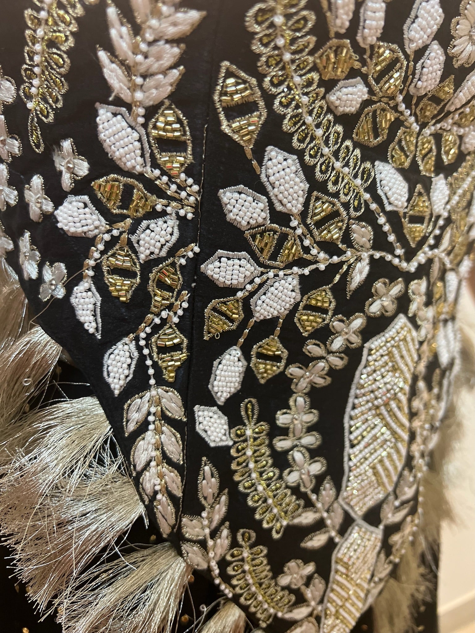 Close-up of an intricately embroidered fabric with gold and white patterns on a black background.