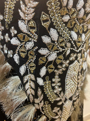 Close-up of an intricately embroidered fabric with gold and white patterns on a black background.