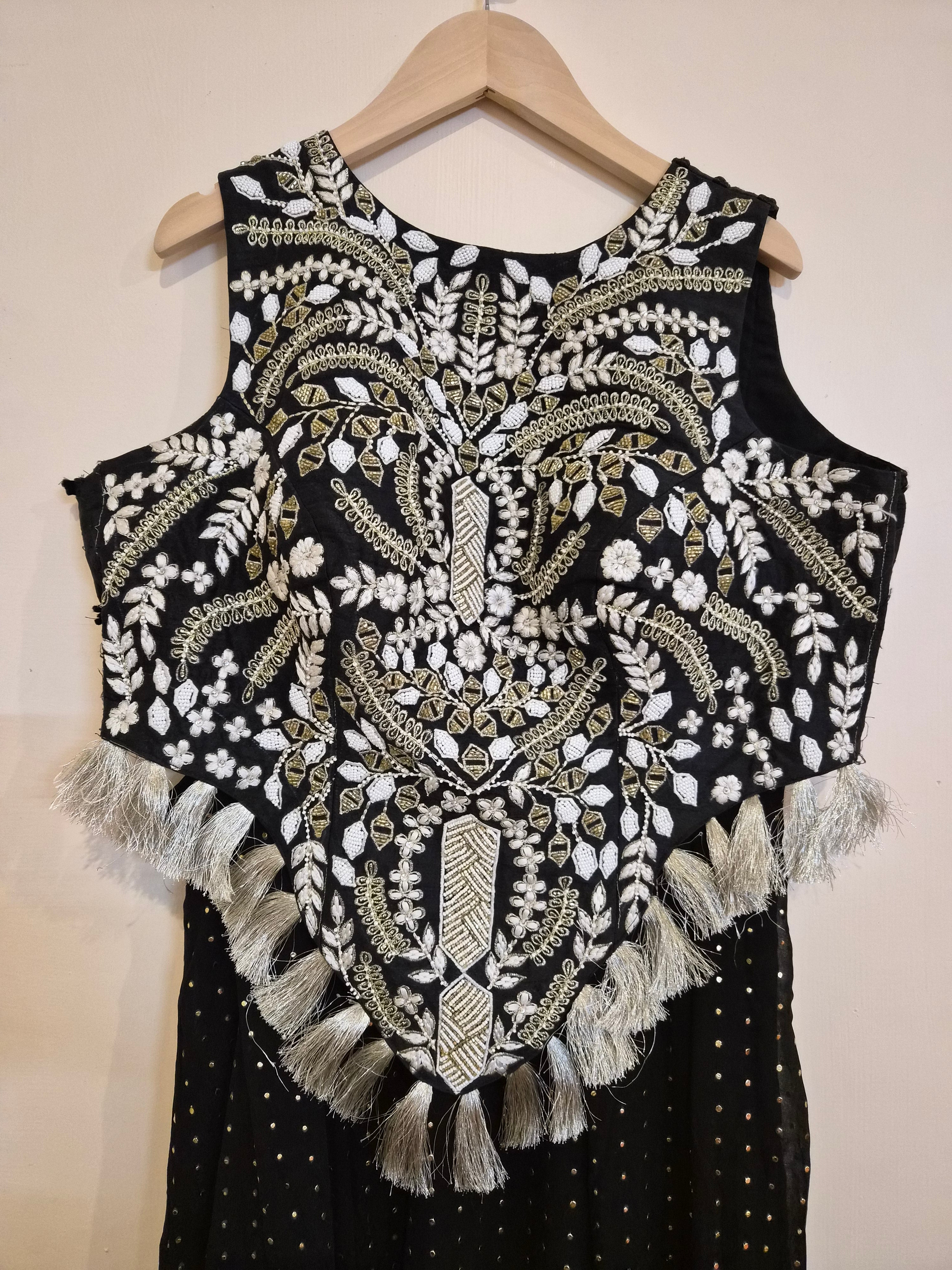 Black sleeveless choli top with intricate white and gold embroidery on a beige background